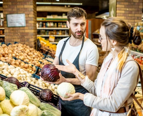 Grocery store employee showing woman a vegetable.