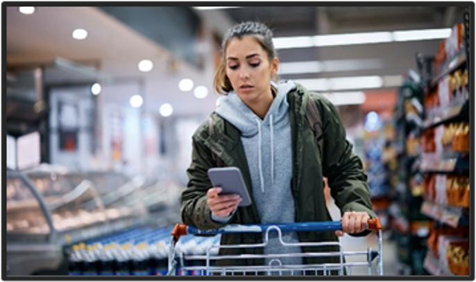 Woman pushing a cart in the grocery store while looking at her phone.