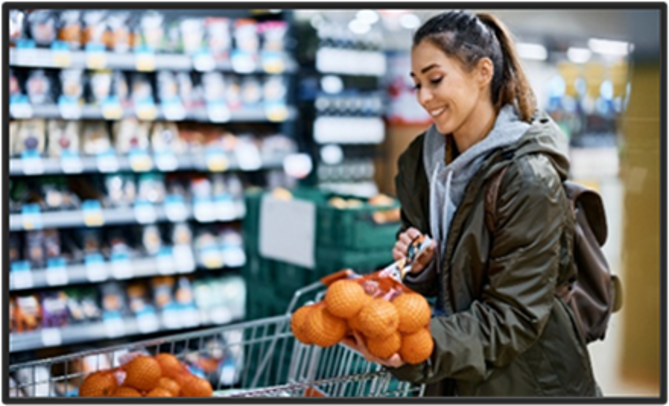 Woman at a grocery store putting a bag of oranges into her cart.